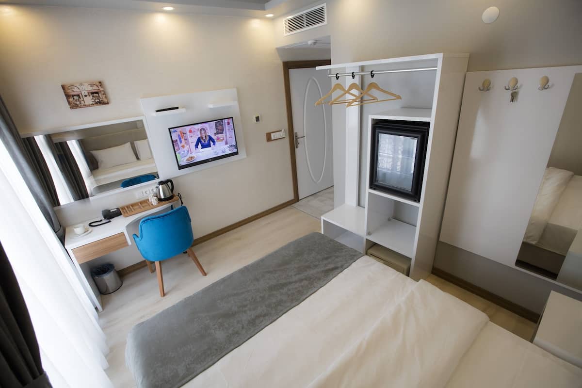 A modern hotel room with a bed, a desk with a chair, a television, and a wardrobe with a mirror.