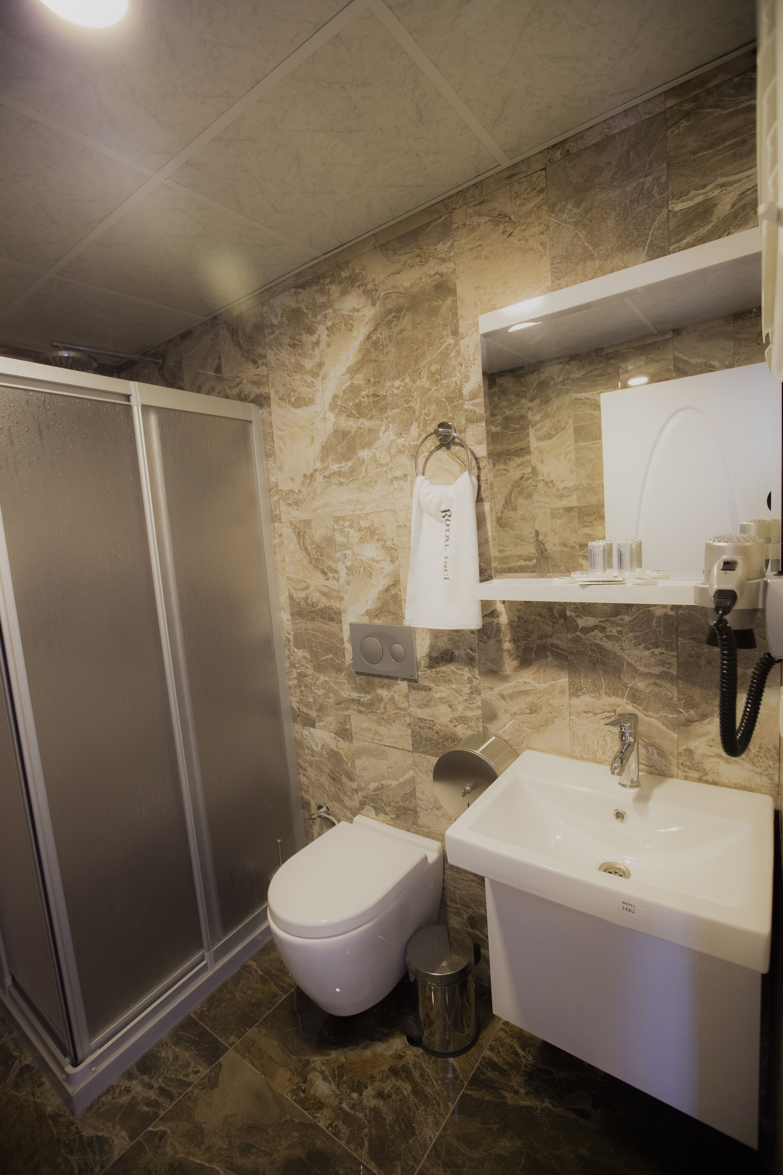 A bathroom with a shower, toilet, sink, and marble walls.