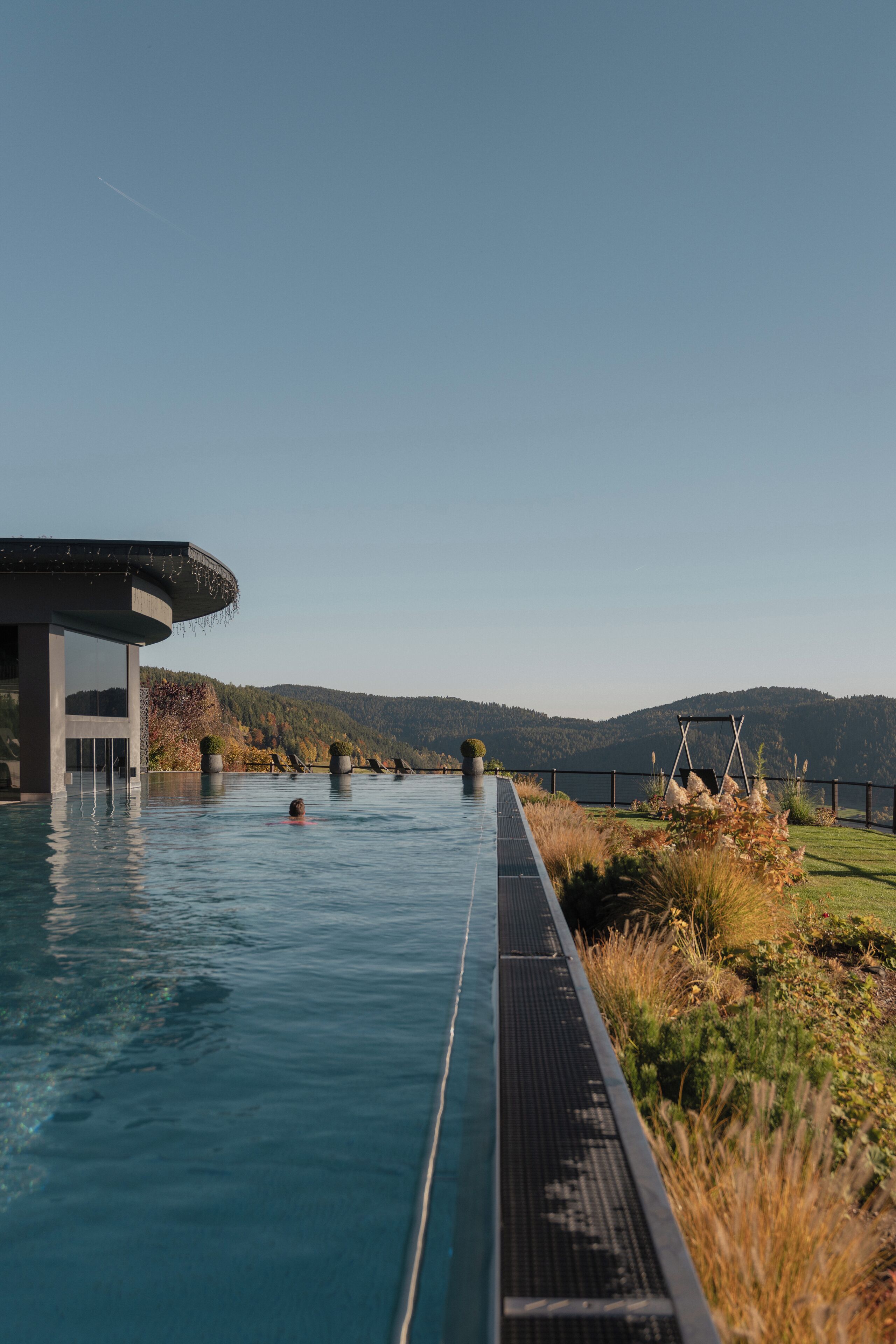 An infinity pool with a view of mountains, a covered area, and lounge chairs.