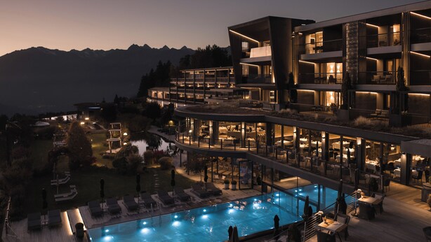 Un hotel moderno con piscina, zona de estar exterior y vistas a la montaña.