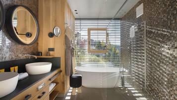Un bagno moderno con due ampi lavabi, uno specchio rotondo, uno sgabello indipendente, una vasca da bagno e una doccia con pareti in vetro.