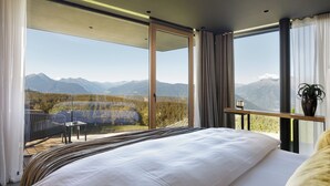 Un dormitorio con una cama grande, un balcón con vistas a montañas y una mesa con una planta.