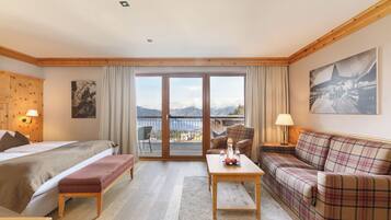 Ein Hotelzimmer mit Bett, einer Sitzecke, einem Tisch und Blick auf Berge durch die Glasdoor.