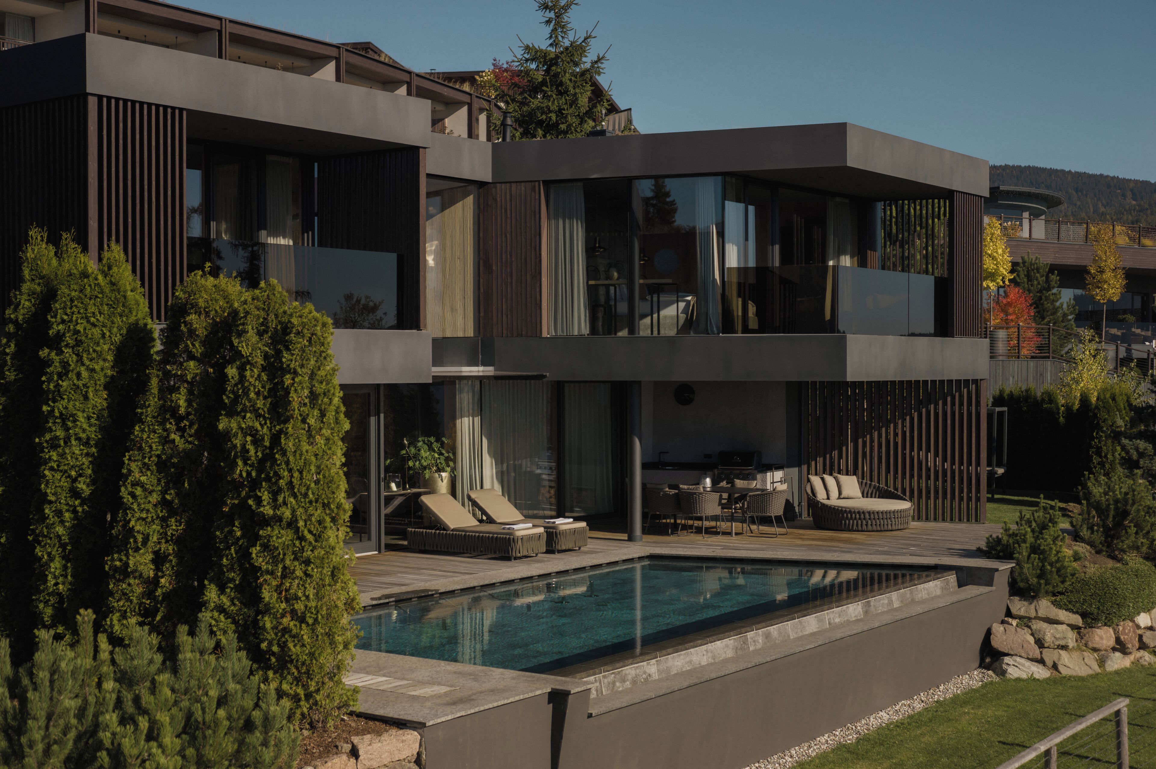 Une maison moderne à deux étages, dotée d’une piscine, d’un espace salon extérieur et offrant une vue sur le paysage environnant.