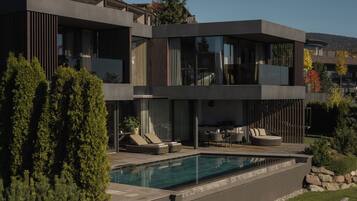 Une maison moderne à deux étages, dotée d’une piscine, d’un espace salon extérieur et offrant une vue sur le paysage environnant.