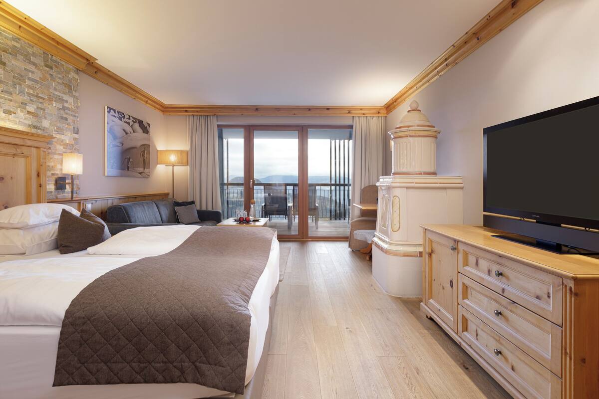 Ett hotellrum med en stor säng, en tv, en byrå i trä och en balkong med utsikt.