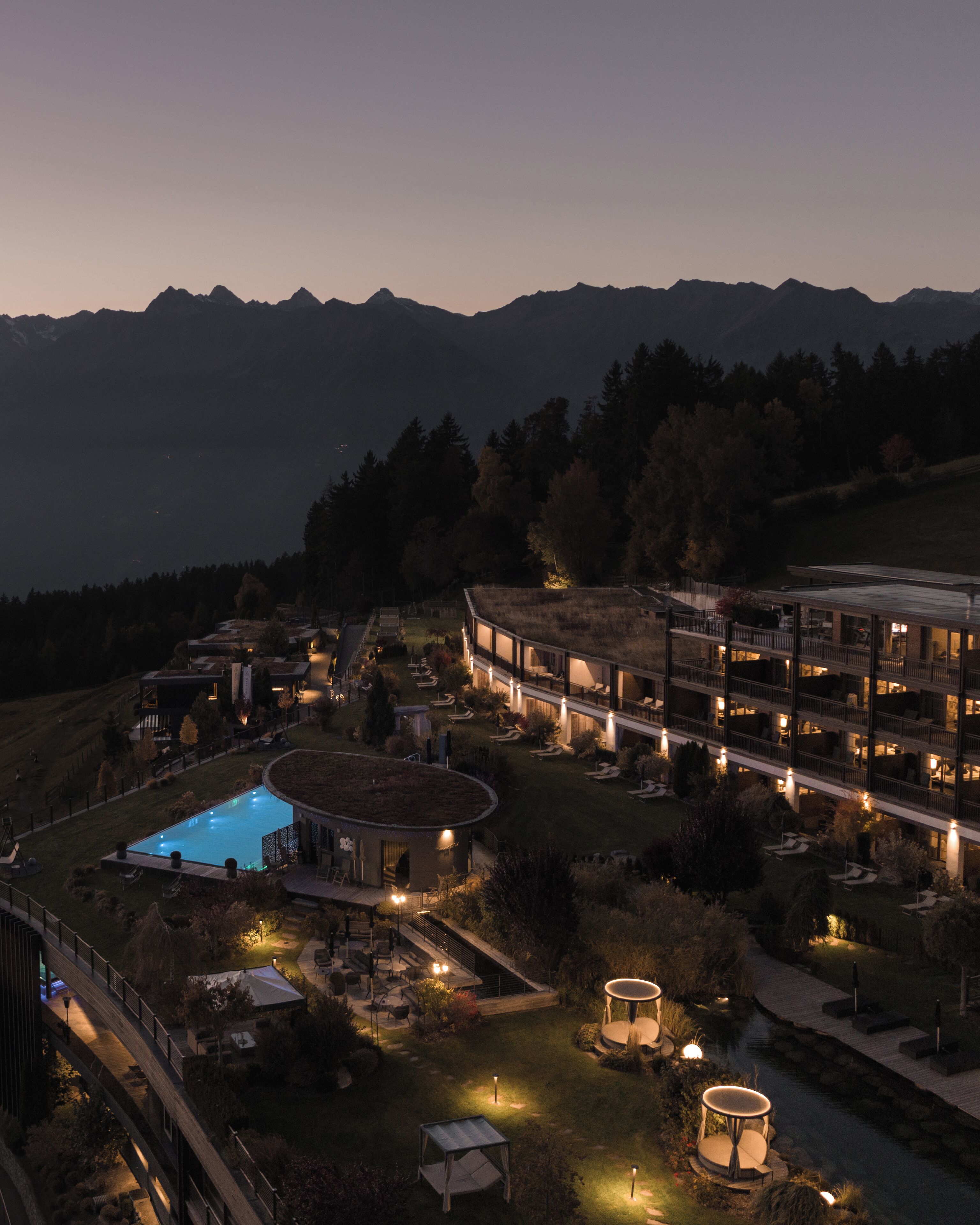 A modern hotel with a pool, outdoor lighting, and a view of mountains.