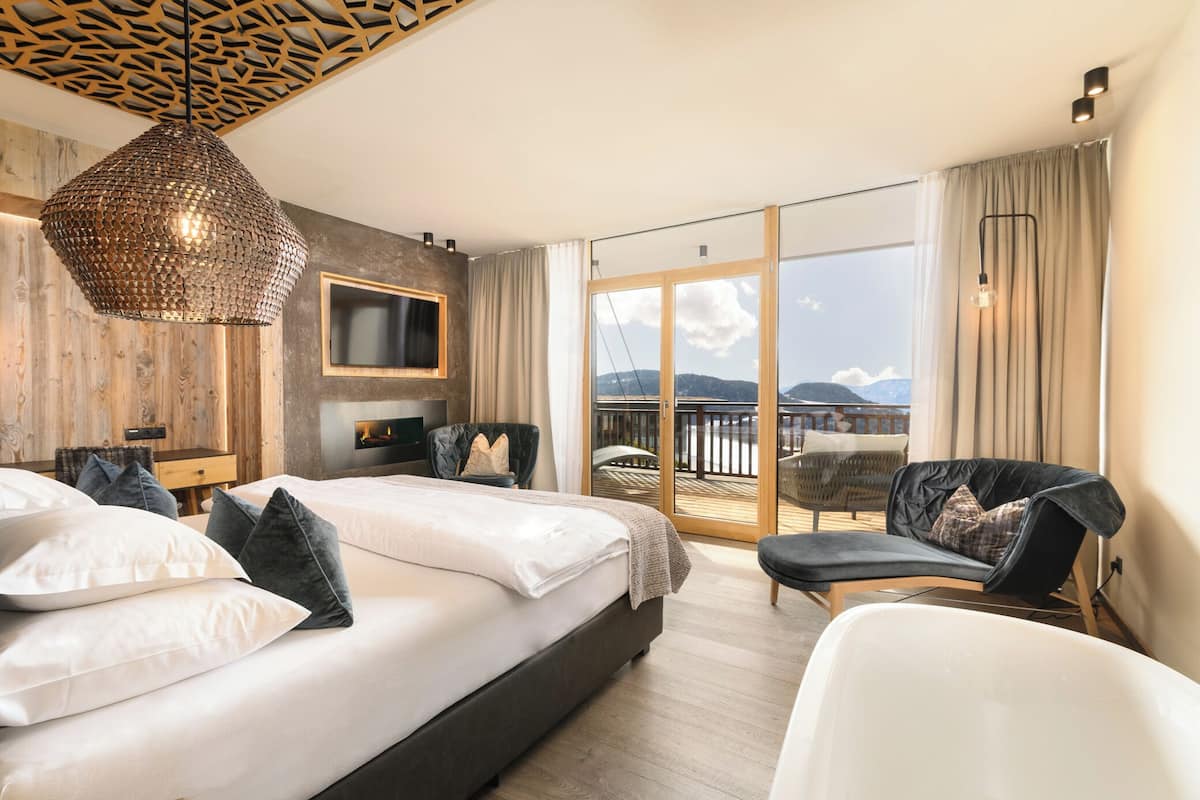 Ett modernt hotellrum med en stor säng, en sittgrupp, en TV som är monterad på väggen och en balkong med utsikt över bergen.