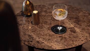 Een ronde tafel met een donker, geribbeld oppervlak, een kaars en een glas met drank.