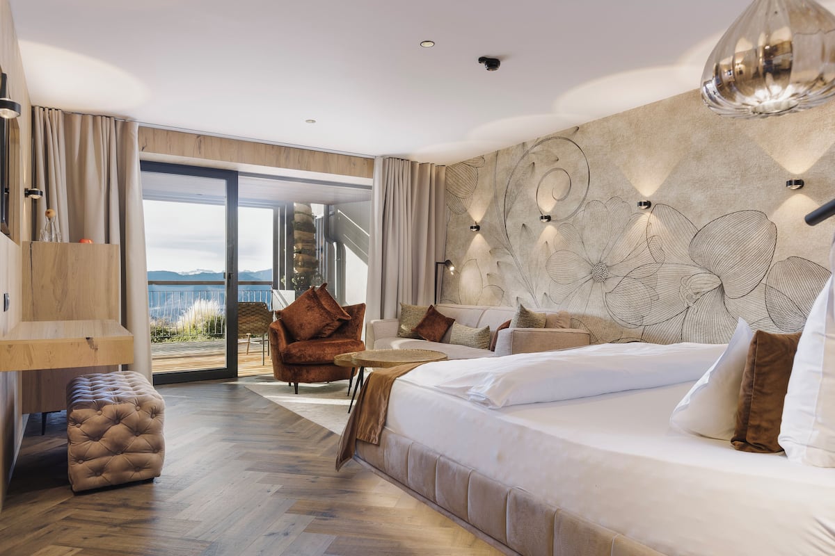 Ett modernt hotellrum med en stor säng, en sittgrupp med soffa och fåtöljer, ett litet runt bord och utsikt över omgivningarna.