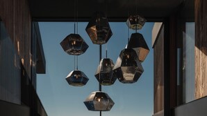 Un interior moderno con suelo de madera, ventanas amplias y lámparas geométricas colgantes.
