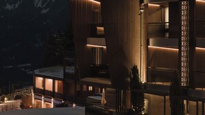 Un hotel moderno con fachada de madera, varios balcones y vistas a montañas nevadas.