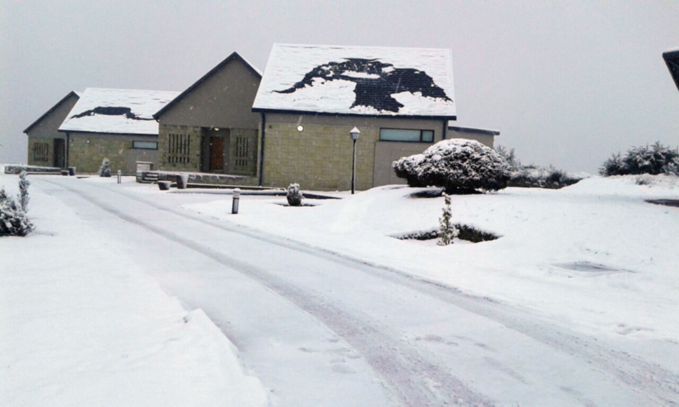Un edificio con techo nevado y camino de entrada pavimentado.
