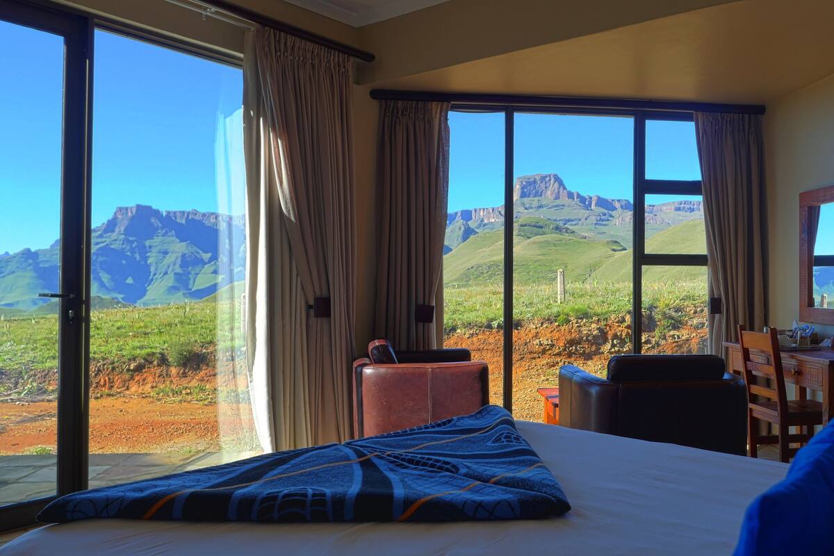 A hotel room with a large bed, a desk, a chair, and a view of mountains.