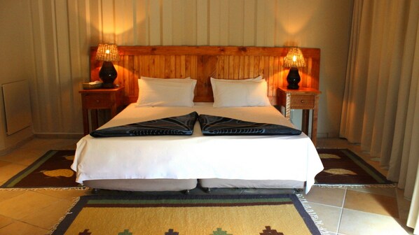 A hotel room with a wooden headboard, two bedside lamps, a bed with white linens, and a decorative rug.