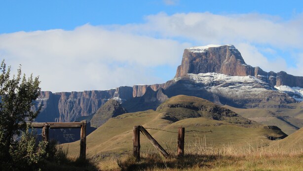 A mountainous landscape with a prominent rock formation and a wooden fence in the foreground. - Witsieshoek Mountain Lodge (Maluti a Phofung)