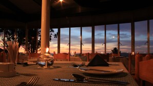 A dining table set for two with a view of the sunset through large windows. - Witsieshoek Mountain Lodge (Maluti a Phofung)