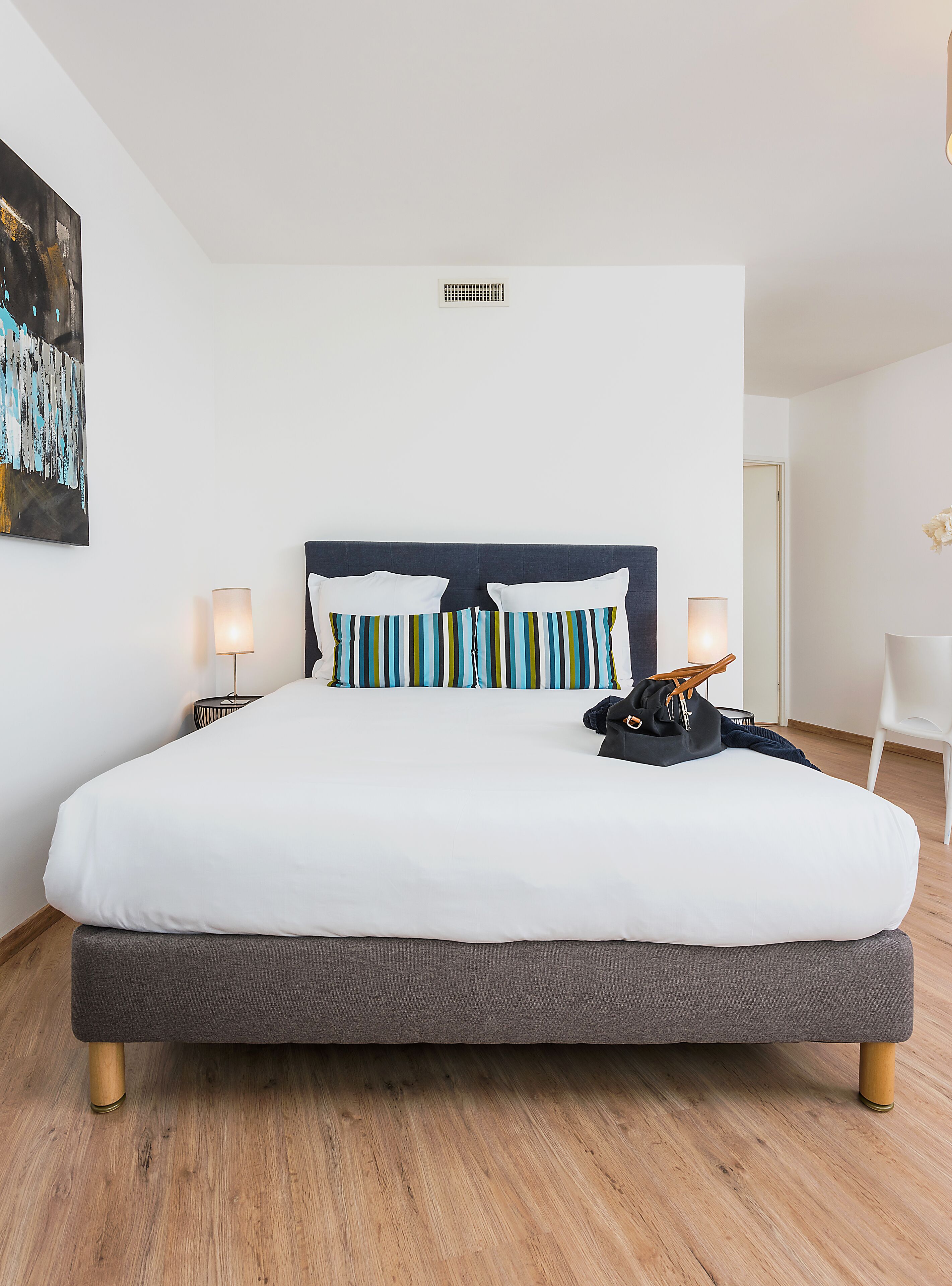 A modern bedroom with a large bed, two bedside lamps, and a decorative pillow arrangement.