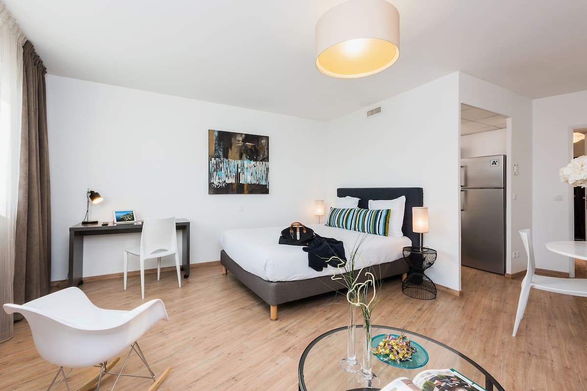 A modern hotel room with a bed, desk, chairs, and a dining area.
