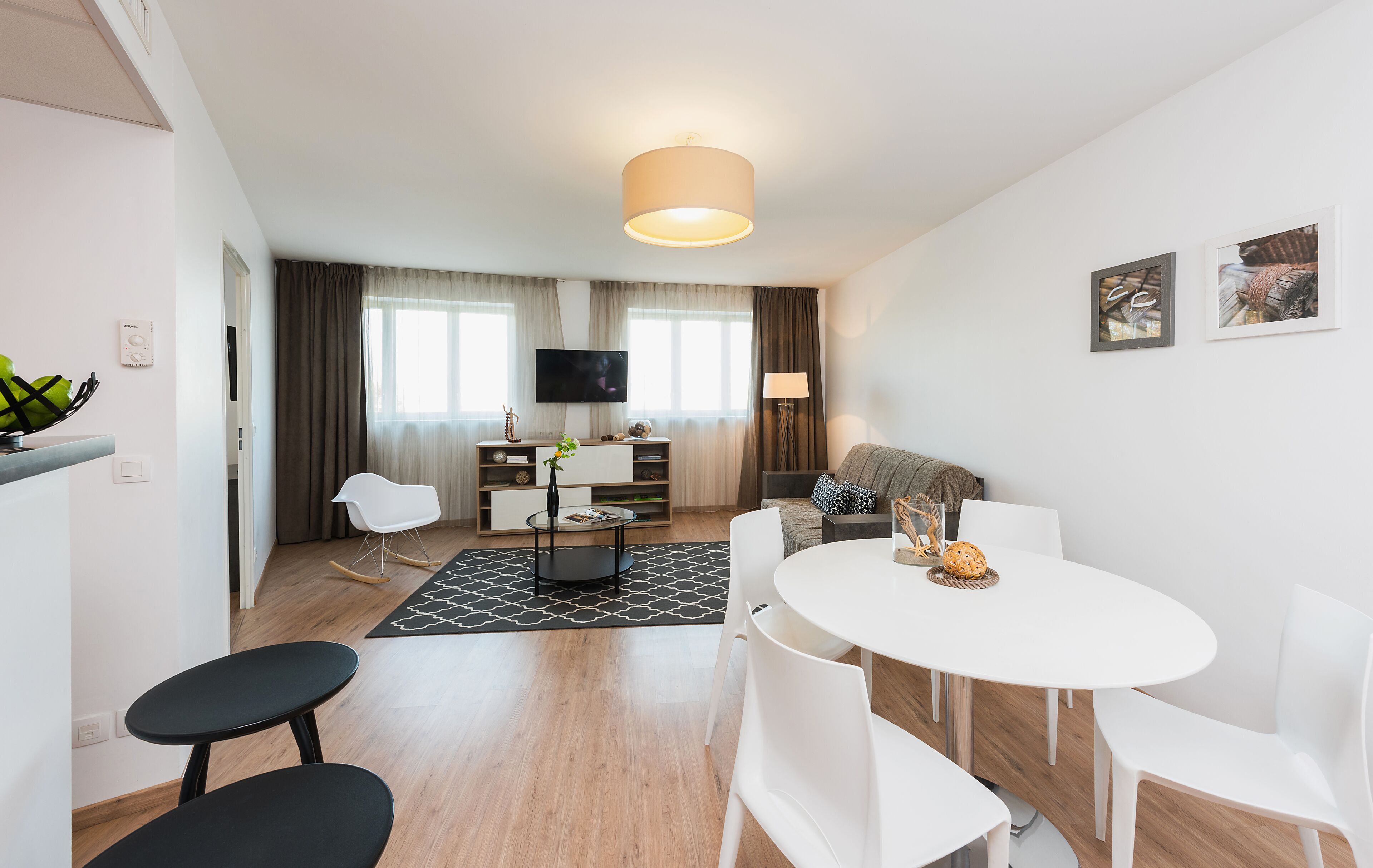 A modern living room with a sofa, a dining table with chairs, a TV, and a lamp.