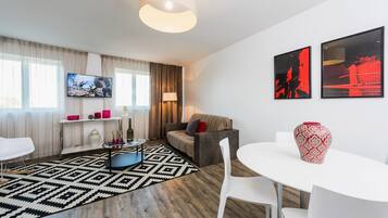 A modern living room with a sofa, a TV, a coffee table, and a dining area.