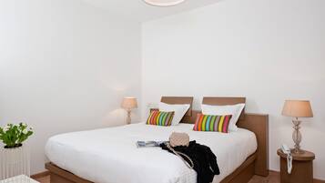 A modern hotel room with a large bed, bedside tables, a small side table, a potted plant, and a lamp.