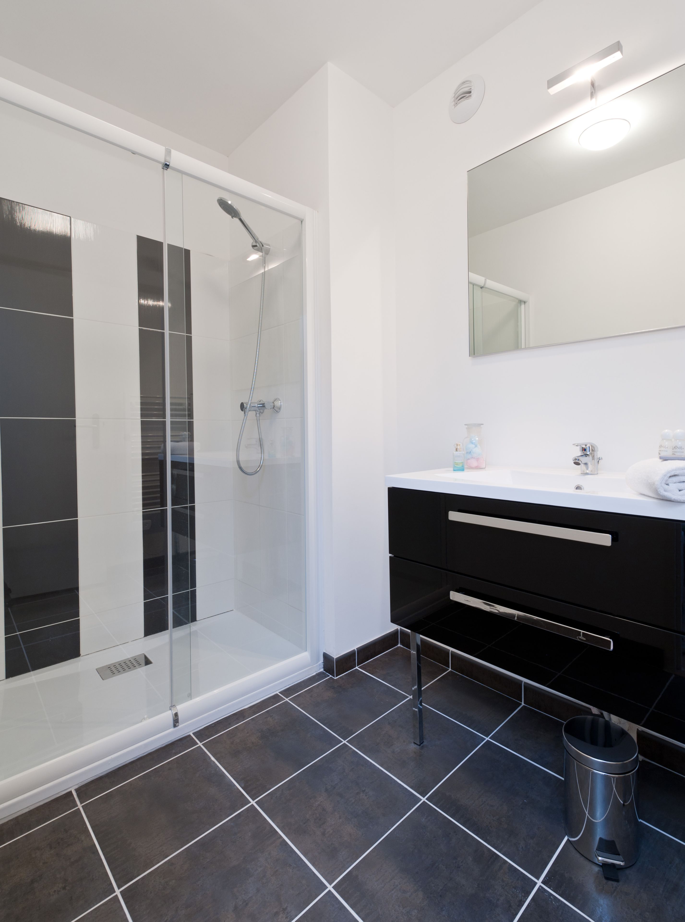 A modern bathroom with a glass-enclosed shower, a white sink with a black cabinet, and a large mirror.