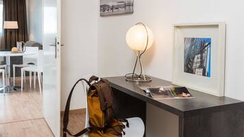 A modern hotel room with a desk, a chair, a lamp, and framed pictures on the wall.