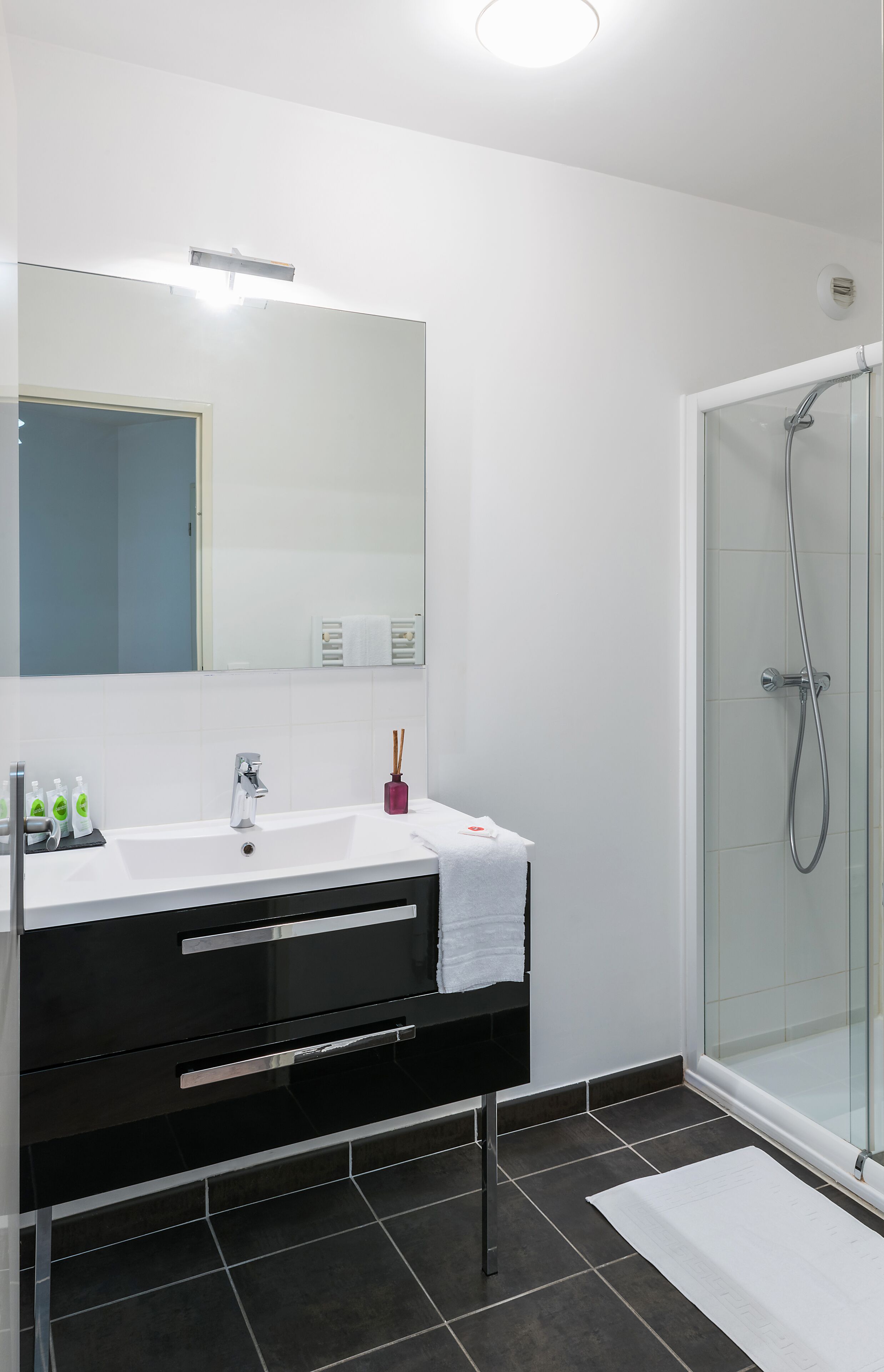 Un baño moderno con lavamanos blanco, tocador negro y cabina de ducha con mampara de vidrio.