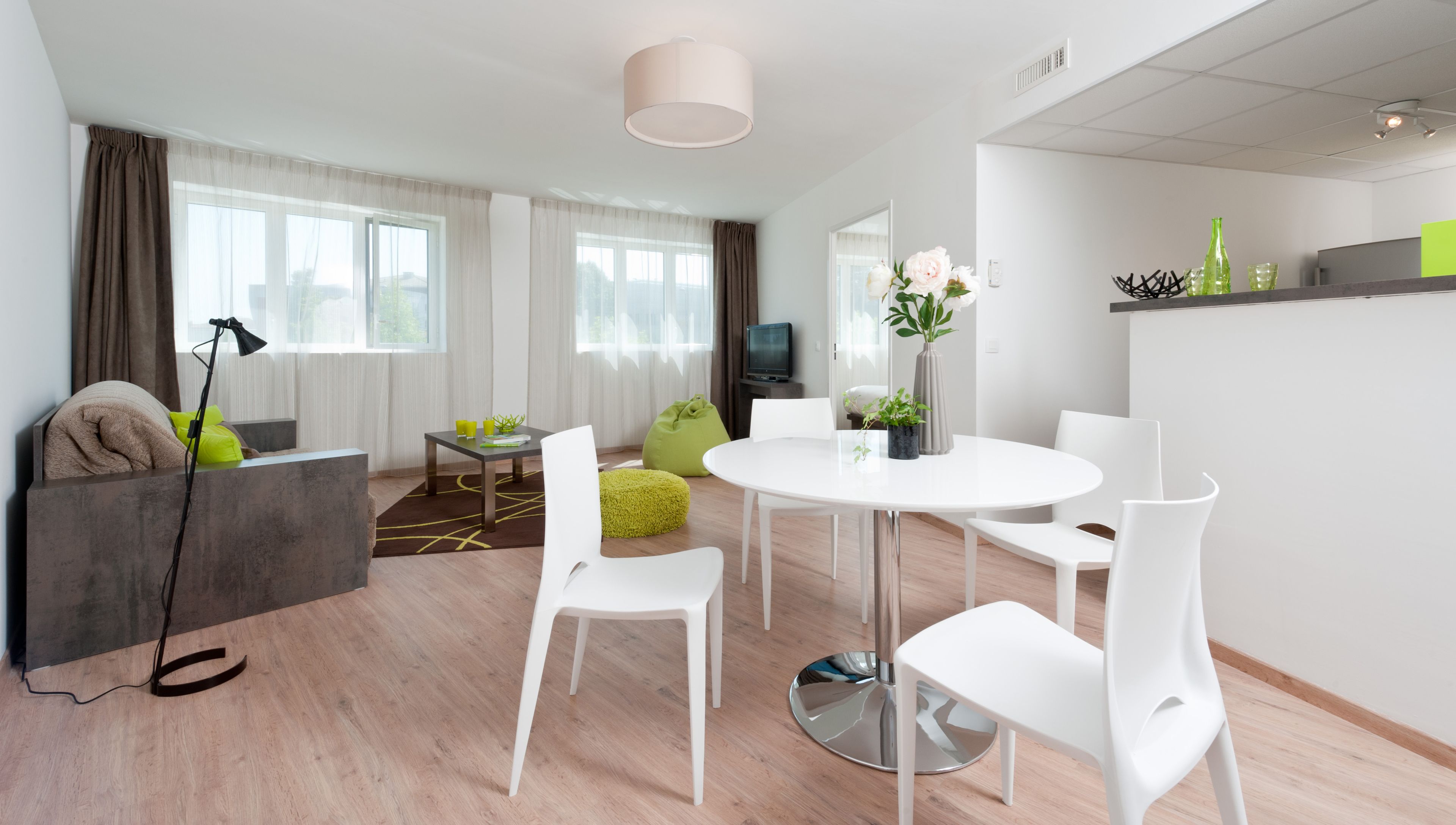 Un salón moderno con un sofá, una mesa de centro y una mesa de comedor con sillas. Hay un televisor sobre un mueble bajo y una ventana con cortinas.