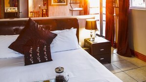 Une chambre d’hôtel avec un grand lit, une table de chevet avec une lampe, un plateau avec des tasses et une cafetière, et une vue sur l’extérieur par une fenêtre.