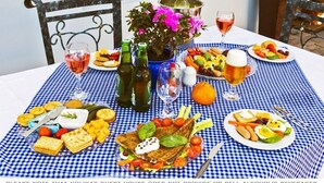 Une table dressée avec une variété d’aliments, notamment du pain, du fromage et des fruits, ainsi que des bouteilles de vin et un vase rempli de fleurs.