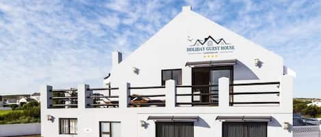 Un bâtiment blanc avec une enseigne indiquant « Maison d’hôtes pour les vacances » et un balcon.