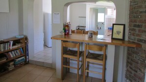 A kitchen with a wooden table and chairs, a bookshelf, and a framed certificate on the wall. - Absolute Leisure Cottages (eNtokozweni)
