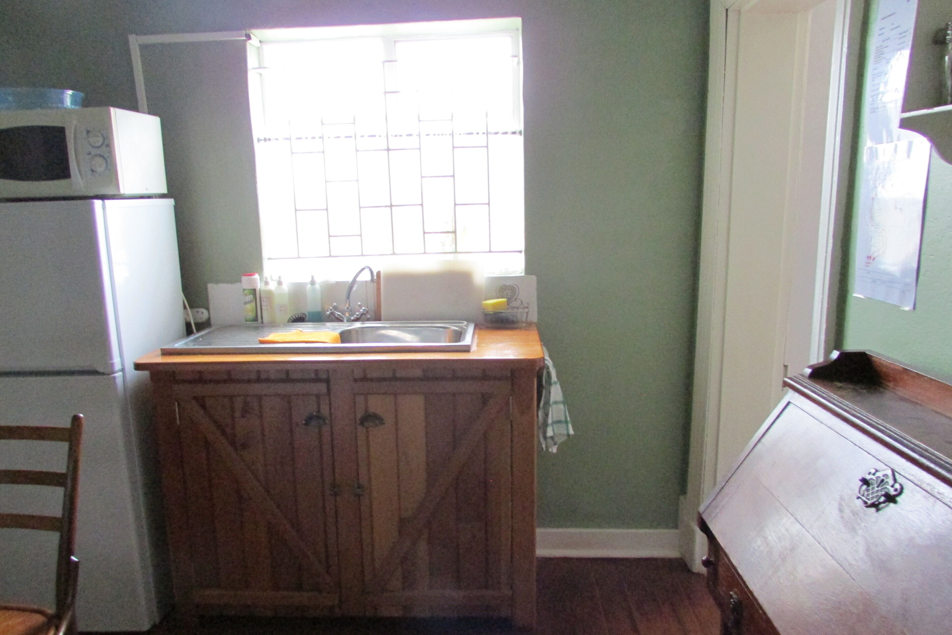 Cocina compacta con un mueble de madera, un microondas, un lavamanos y una ventana con persianas.