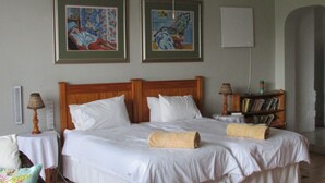 A neatly made bed with white linens and two rolled towels, a wooden headboard, a bedside table with a lamp, and a bookshelf with books. - Absolute Leisure Cottages (eNtokozweni)