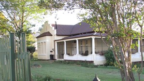 A two-story house with a porch, a fenced yard, and a garden. - Absolute Leisure Cottages (eNtokozweni)