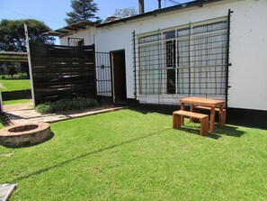 Un pequeño edificio blanco con un patio amurallado, un banco de madera y un jardín pequeño.