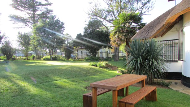A wooden picnic table in a well-maintained grassy yard with a thatched-roof building in the background. - Absolute Leisure Cottages (eNtokozweni)