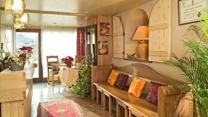 A cozy room with a wooden bench, a table with chairs, and a window with curtains. - Hotel Restaurant Robichon (Loray)