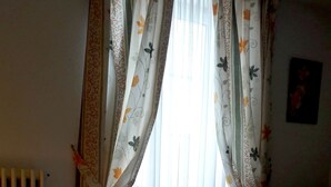 A hotel room with a bed, curtains, a radiator, and a wall with a picture. - Hotel Restaurant Robichon (Loray)