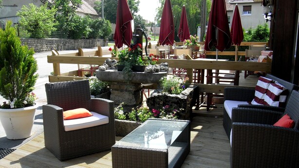 An outdoor seating area with wicker furniture, stone planters with flowers, and red umbrellas. - Hotel Restaurant Robichon (Loray)