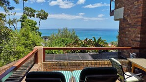 A balcony with two chairs and a table, overlooking a coastal view with the ocean and a clear sky. - Magic Camps Bay (Cape Town)
