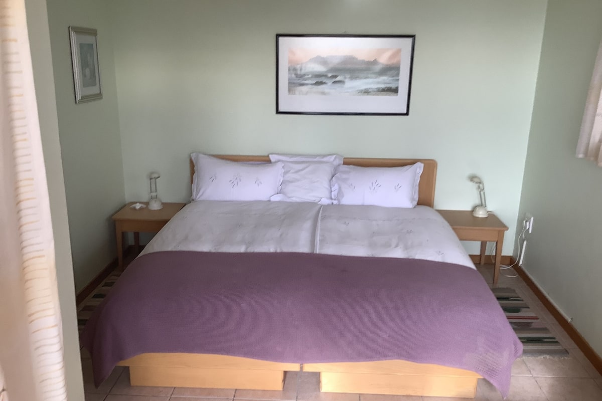 A neatly made bed with a purple blanket, a wooden headboard, and a framed picture on the wall.