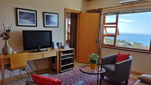 A living room with a TV, a sofa, a coffee table, a rug, and a view of the sea. - Magic Camps Bay (Cape Town)