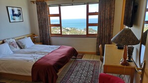 A bedroom with a bed, a desk, a chair, a TV, and a view of the sea. - Magic Camps Bay (Cape Town)