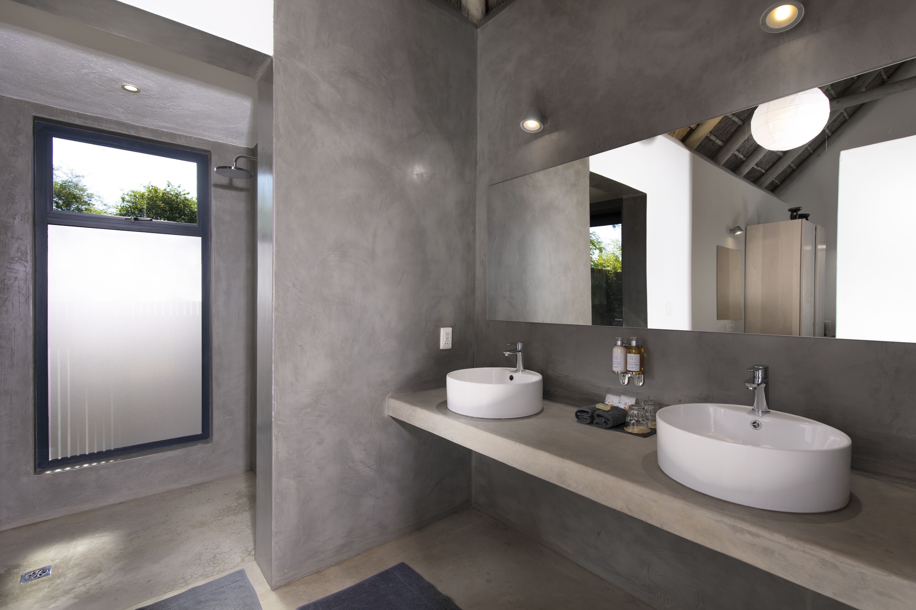 A modern bathroom with two sinks, a large mirror, and a skylight.
