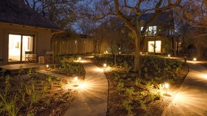 Een goed verlicht tuinpad dat leidt naar een gebouw met een rieten dak en een grote glazen deur.