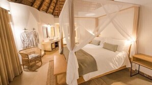 Een slaapkamer met een hemelbed, nachtkastje, stoel en spiegel.