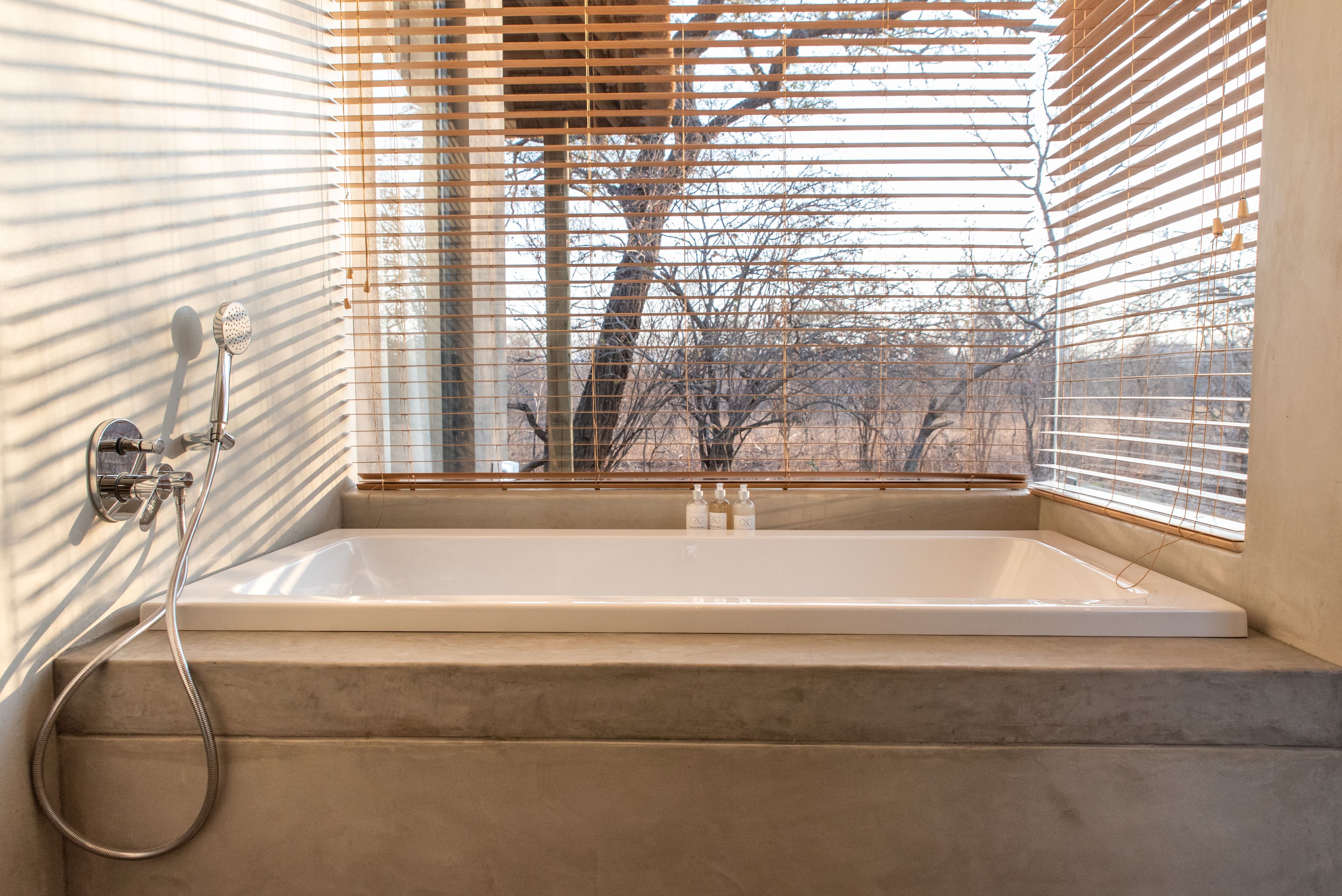 Ein modernes Badezimmer mit einer Badewanne, einer Dusche und einem Fenster mit Jalousien.